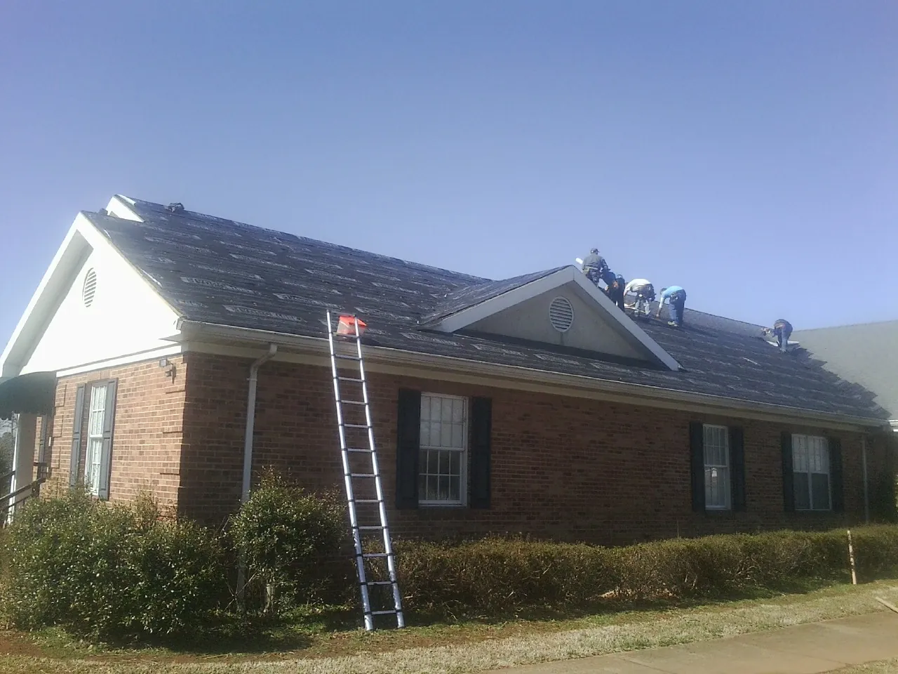 Crew tearing shingles off a brick ranch roof with a ladder set — Metal Roof Repair work by our crew in Somerset
