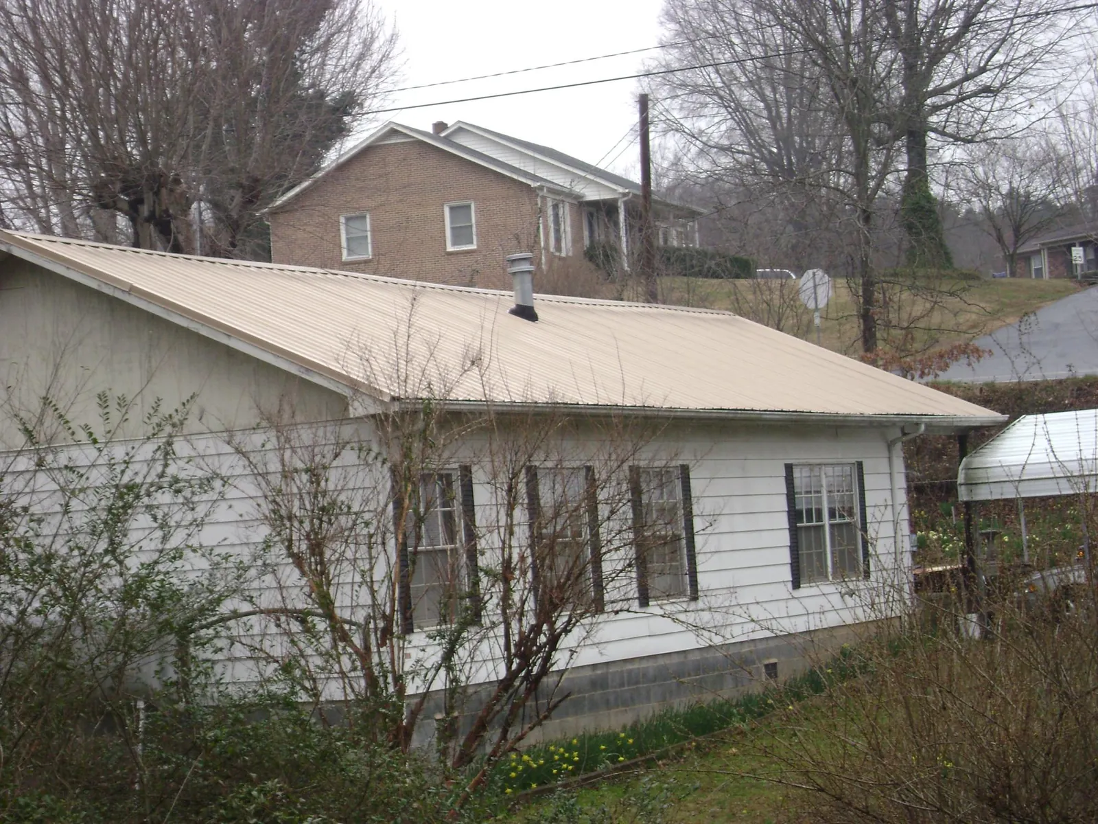 Tan metal roof on a white sided house set into a hillside — Commercial Roofing by Roofing Brothers in Somerset